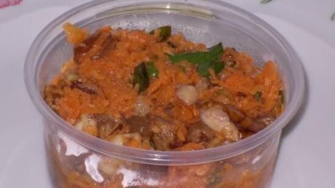 Ein durchsichtiger Behälter mit Möhrensalat steht auf einem blumengemusterten Teller und zeigt frische, geriebene Karotten.