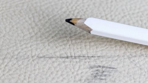 Ein Bleistift liegt auf Kunstleder, während er eine Markierung hinterlässt, die entfernt werden soll.