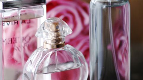 Drei Parfümflaschen stehen auf einem Holztisch, umgeben von rosa Rosenblüten, die den Duft vom Lieblingsparfum im Deo unterstreichen.