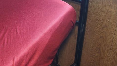 Ein rotes Bettlaken liegt über einem verstellbaren Matratzenrost, der an einem Holzbettgestell befestigt ist.