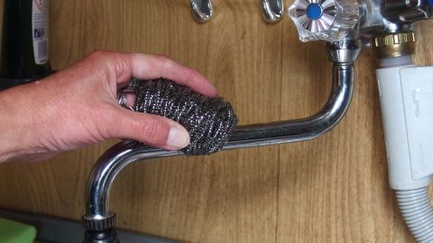 Verschmutzte Silikonfugen und verkalkte Armaturen ohne teure Putzmittel reinigen: Ein Stahlschwämmchen (Topfkratzer) wirkt Wunder. Eine Hand reinigt eine verkalkte Armatur mit einem Scheuerschwamm, um Ablagerungen in der Küche zu entfernen.