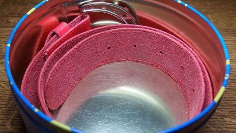 Ein rosa Gürtel liegt ordentlich in einer runden, bunten Dose, die als Aufbewahrungsort dient.