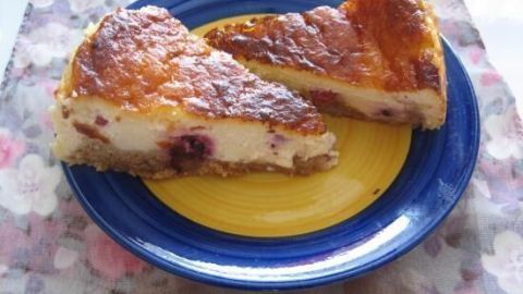Zwei Stücke Käsekuchen mit Mandarinenstückchen liegen auf einem gelben Teller, umgeben von einer blumigen Tischdecke.