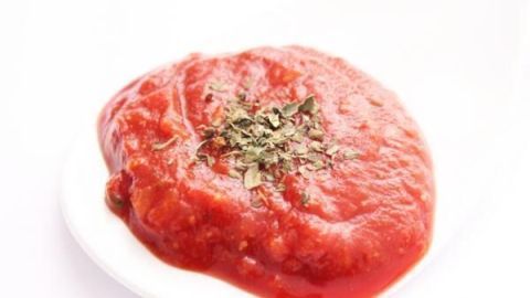 Tomatensoße liegt auf einem weißen Löffel, belegt mit getrockneten Kräutern, ideal für Pizzasoße oder Pizzaiola.