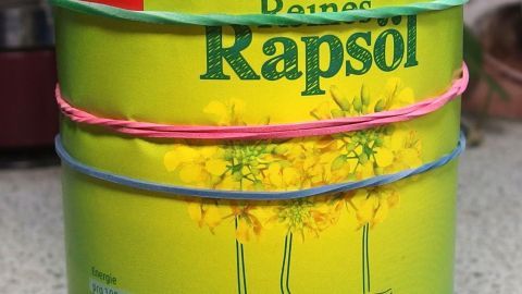 Eine grüne Ölflasche mit Gummibändern zur besseren Handhabung steht auf einer Arbeitsfläche in einer Küche.
