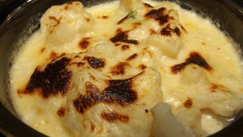 Blumenkohlstücke in cremiger Käsesauce sind goldbraun überbacken und in einer schwarzen Auflaufform angerichtet.