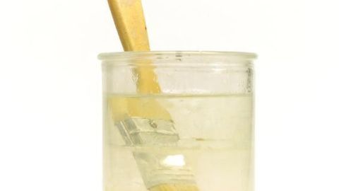 Ein Pinsel mit rotem Griff steht in einem Glas mit Terpentin, umgeben von einem weißen Hintergrund.