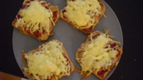 Vier Pizza Toasts sind mit geschmolzenem Käse und Tomatensauce bedeckt und liegen auf einem grauen Teller.