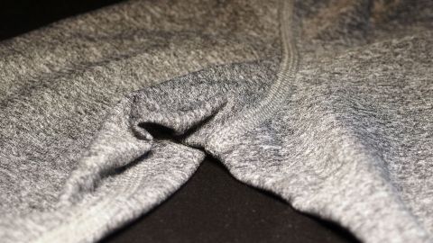 Manchmal verschwindet Schweißgeruch in der Kleidung nach dem Waschen nicht. Hier hilft Essigwasser. Ein graues Kleidungsstück liegt auf einem dunklen Untergrund und zeigt eine Falte, die auf Schweißgeruch hinweisen könnte.