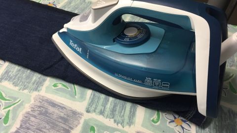 Ein Dampfbügeleisen steht auf einer Jeanshose, während es gebügelt wird, auf einem farbenfrohen Tischdeckenmuster.