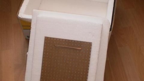 Eine Kühlbox steht offen auf einem Holzboden, während der Deckel daneben liegt. Der Kontext zeigt einen Raum mit Vorhängen.