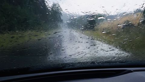 Regenbogen perlt über die Windschutzscheibe eines Fahrzeugs, während die Straße nass und sichtbar abgelegen ist.