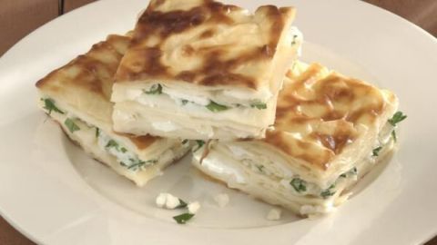 Auf einem Teller liegen frisch gebackene Stücke von Börek, leicht goldbraun gebräunt, mit Kräutern gefüllt.