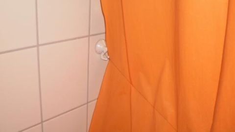 Ein oranger Duschvorhang hängt an einer weißen Wand, sieht glatt aus und scheint nicht zu kleben.
