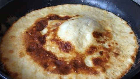 Um einen dicken und lockeren Pfannkuchen zu bekommen, den Teig vor dem Backen etwa 15 Minuten ruhen lassen Ein lockerer Pfannkuchen bräunt sich in einer Pfanne, während er auf dem Herd zubereitet wird.