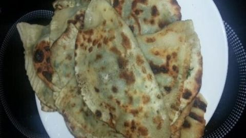 Gözleme liegen gestapelt auf einem weißen Teller, frisch gebacken in der Pfanne, mit braunen Stellen, vor dunklem Hintergrund.