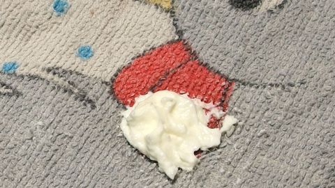 Ein graues Kleidungsstück mit einem Obstfleck aus heller, klebriger Substanz ist zu sehen.