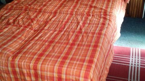 Eine Decke aus alten Bettbezügen liegt ordentlich auf einem Bett in einem Holzverkleidung Raum, umgeben von Bodenläufern.