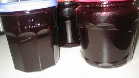 Dunkle Aronia-Apfel-Marmelade in Gläsern steht auf einer Oberfläche, während der Hintergrund verschwommen ist.