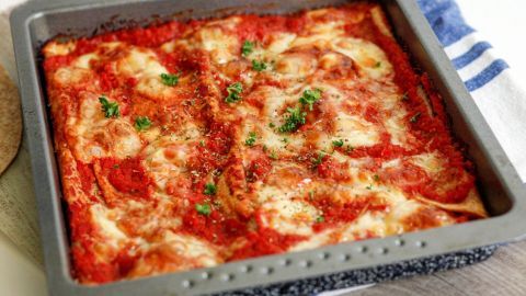 Ein quadratisches Blech mit überbackenen Wraps in Tomatensauce und Käse, garniert mit frischer Petersilie.