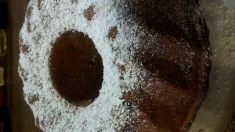 Ein schokoladiger Bananen-Nusskuchen mit Puderzucker steht auf einem Teller, umgeben von einer Holzoberfläche.
