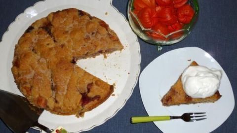 Ein Apfelkuchen aus Weizen und Buchweizen steht auf einem Teller, während ein Stück mit Sahne serviert wird, umgeben von frischem Obst.