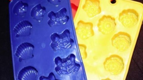 Bunte Silikonformen liegen auf einer dunklen Oberfläche und dienen zum dekorativen Servieren von Kräuterbutter.