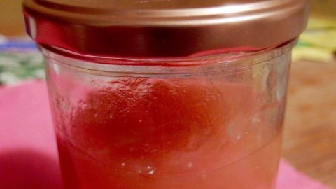 Ein Glas Kürbismarmelade mit Ananas und Kokosmilch steht auf einem Tisch, umgeben von einem bunten Tuch.