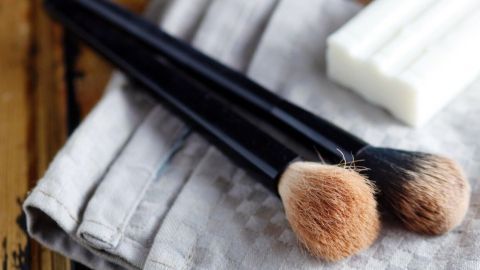 Zwei Make-up-Pinsel liegen auf einem grauen Tuch, während eine Kernseife daneben für die Reinigung bereitsteht.