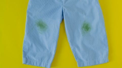 Blaues Kinderhosenpaar liegt auf einem gelben Hintergrund, mit grünen Grasflecken auf den Knien.