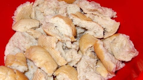 Zerreißene Brötchenstücke ruhen in einer roten Schüssel, bereit für die Zubereitung des Semmelauflauf Scheiterhaufens.