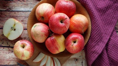 Runde Äpfel liegen in einer Holzschüssel, während ein frischer Apfel halbiert und neben einer Schneidebene platziert ist.