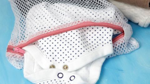 Eine Babykleidung mit Sternenmuster liegt in einem Wäschenetz, bereit zum Knöpfen waschen, auf einer blauen Unterlage.