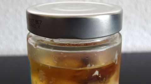 Ein Glas mit altem Speiseöl steht auf einem Tisch, es enthält trübes Öl, das entsorgt werden muss.