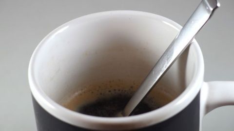 Eine Tasse Kaffee steht auf einem Tisch, der silberne Löffel ragt hinein, der Kaffee wirkt heiß und frisch.