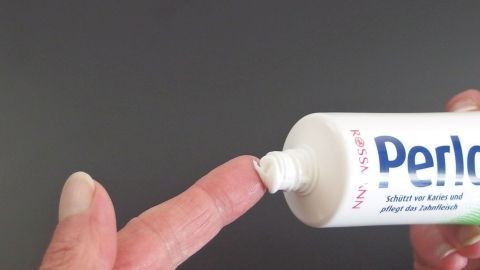 Eine Hand trägt Herpes-Creme auf den Finger auf, um Herpes vorzubeugen, vor einem neutralen Hintergrund.