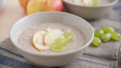In einer Schüssel liegt cremiger Haferbrei, garniert mit Apfel- und Traubenstücken, umgeben von frischen Äpfeln.