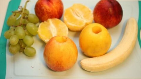 Bunte Früchte wie Äpfel, Trauben und Bananen liegen auf einem Schneidebrett, bereit für die Zubereitung von Smoothies auf Vorrat.