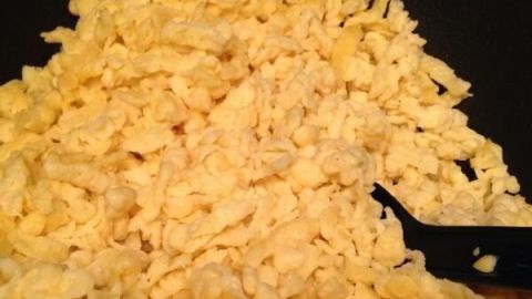 Spätzle braten in einer Pfanne, während ein schwarzer Pfannenwender danebenliegt, bereit zum Wenden der Nudeln.