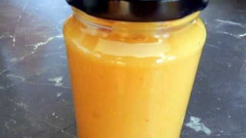 Ein Glas Quitten-Orangenmarmelade steht auf einer dunklen Arbeitsfläche und wartet auf den Genuss.