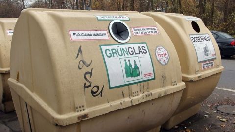 Altglascontainer stehen am Straßenrand; ein Container trägt das Schild "GRÜNGLAS" mit Abbildungen von Flaschen.