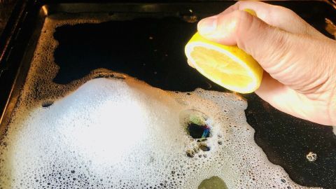 Eine Hand drückt eine Zitronenscheibe über einem schäumenden Backofenreiniger, um den Backofen-Geruch zu entfernen.