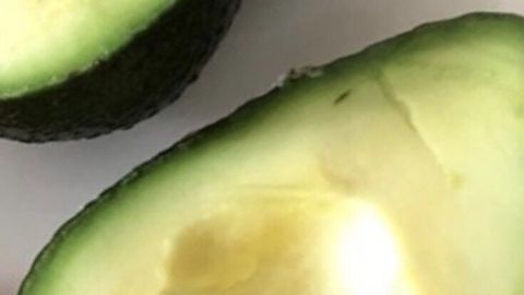 Eine geschnittene Avocado liegt auf einem weißen Teller, die cremige Frucht präsentiert sich offen mit braunem Kern.