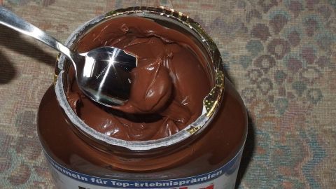Eine geöffnete Nutella-Glas mit einem Teelöffel, das cremige Schokoladenaufstrich wird auf einem Tisch präsentiert.