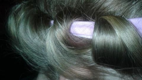 Helle, lockige Haare sind in ein lila Stirnband gewickelt, offensichtlich für ein Locken-Styling ohne Hitze, in Innenumgebung.