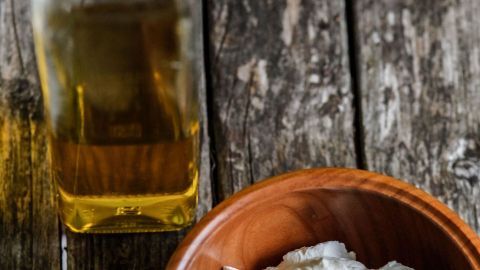 Ein Schüsselchen mit einer cremigen Mischung aus Eigelb steht auf einem Holztisch, daneben eine Flasche Olivenöl und ein Ei.