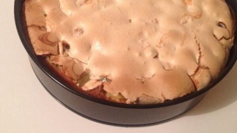 Ein Stachelbeerkuchen mit goldbrauner Baiserhaube steht auf einer weißen Fläche und wirkt frisch gebacken.