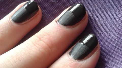 Schwarzer matter Nagellack bedeckt Fingernägel auf violettem Stoffhintergrund, der Textur und Tiefe zeigt.