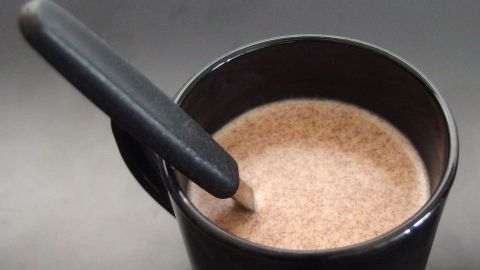 Eine schwarze Tasse mit warmer, schaumiger heißer Schokolade und einem Löffel in einer dunklen Umgebung.