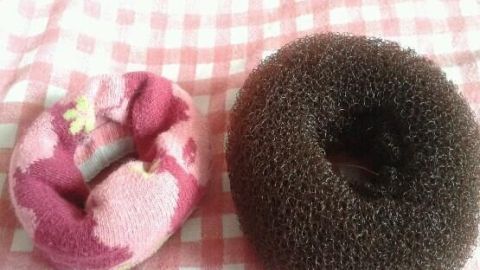 Eine gerollte, bunte Socke liegt links von einem braunen Duttkissen auf einem rot-weißen Karomuster.